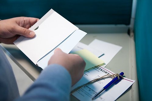 En person står i ett röstbås och lägger en valsedel i ett kuvert.