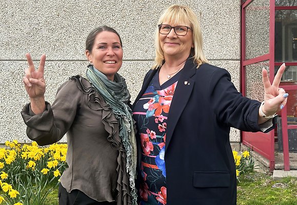 Foto på stadsbyggnadsdirektör Carina Molin och kommunstyrelsens ordförande Stina Lundgren (M), som glada står utanför kommunhuset. En rabatt med påskliljor syns i bakgrunden.