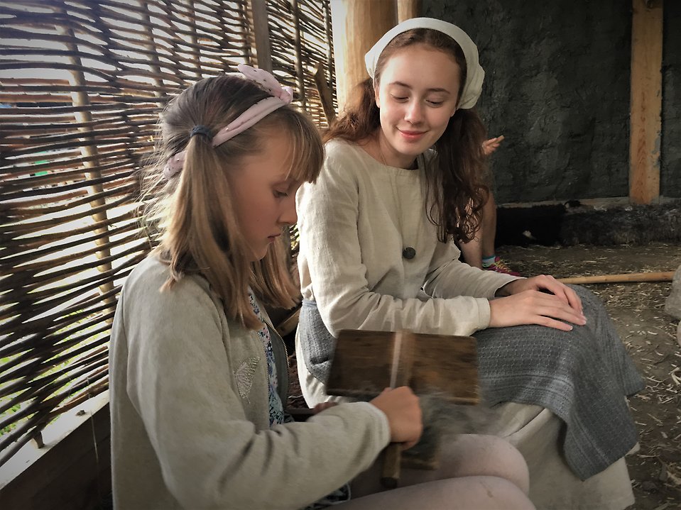 Två flickor kardar ull i järnåldersbyn