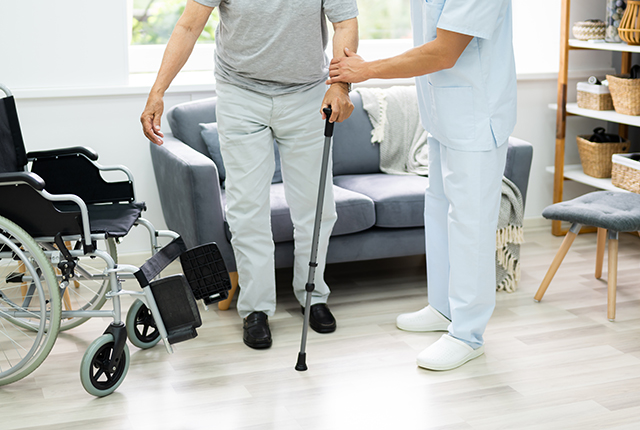 Senior man med krycka får stöd av omsorgspersonal