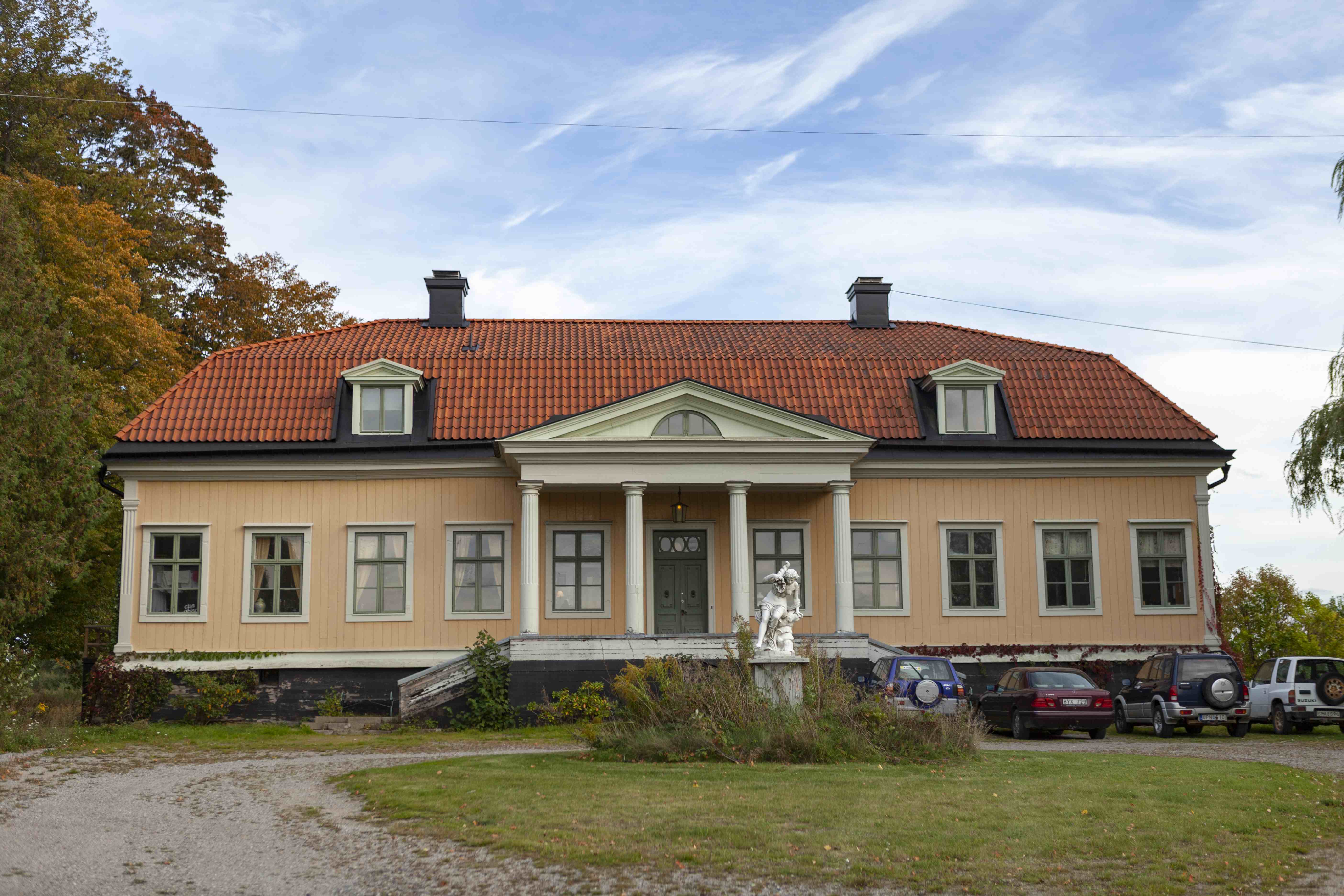 Ett herrgårdshus. På framsidan står bilar parkerade.