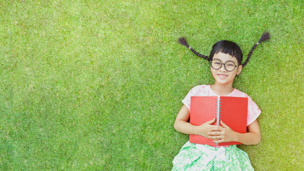 Flicka som ligger i gräset med en bok