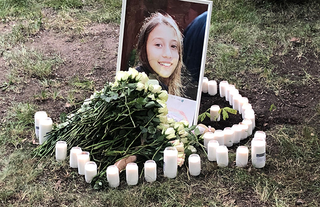 Foto av minnesplats med foto av ung flicka, levande ljus och blommor.