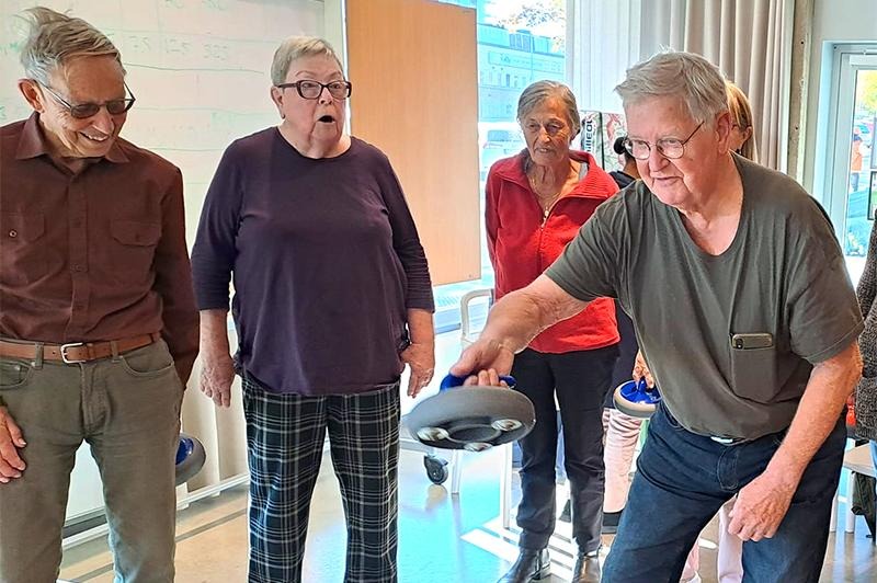 Glada äldre personer spelar inomhuscurling.