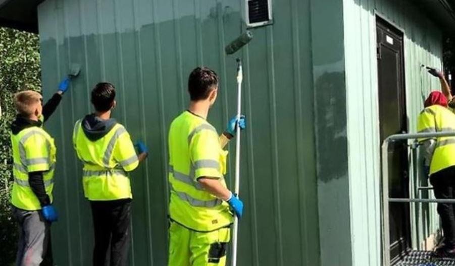Feriepraktikanter som målar ett hus grönt