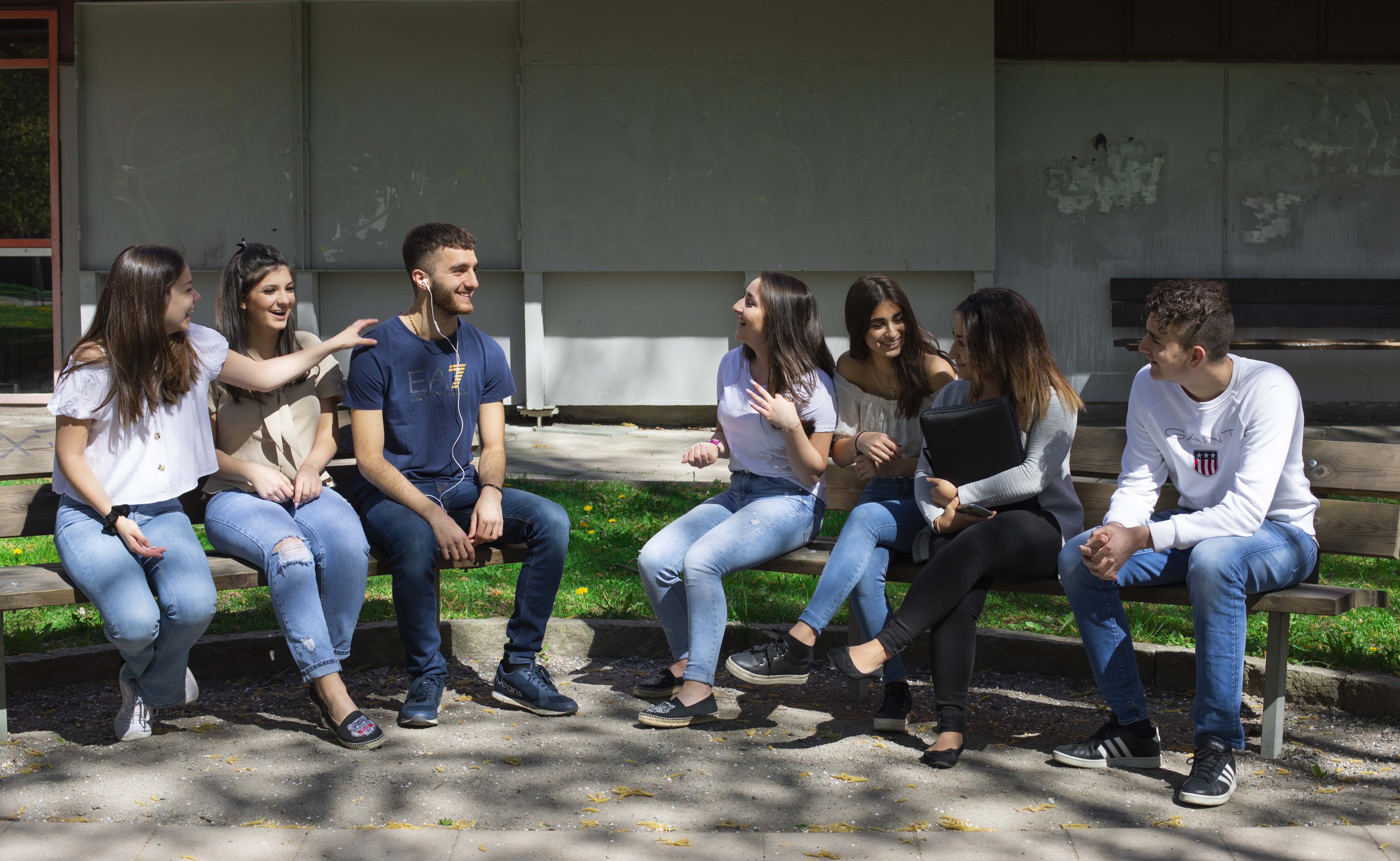 Elever från ett gymnasium i Botkyrka sitter på en bänk.