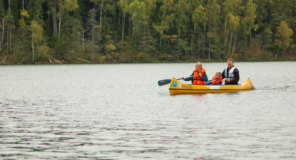 Tre personer, två vuxna och ett barn i en kanot. Skog i bakgrunden.