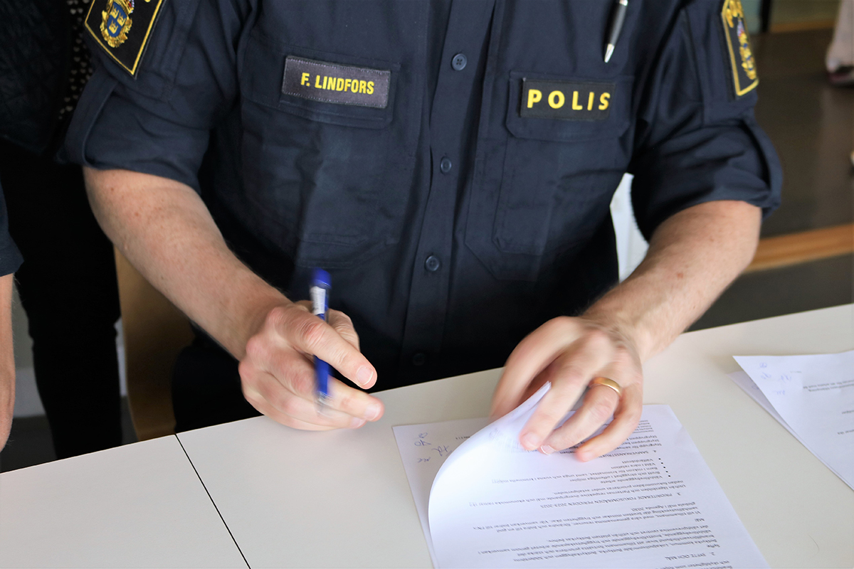 En polisman skriver under ett avtal på ett skrivbord i kontorsmiljö.