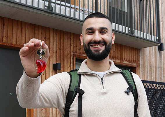 En man, som ser glad ut, håller en nyckelring med ett stort rött hjärta och visar sina hemnycklar 