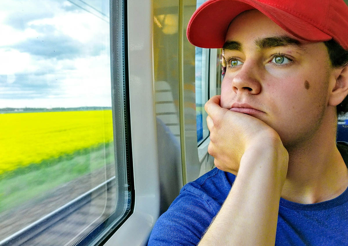 Ung kille med keps tittar ut genom tågförster. Räls och natur syns utanför fönstret.