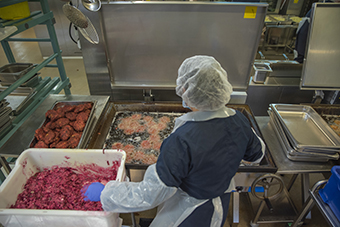 Miljön är Bosphorus matfabrik i Norsborg där en anställd i anticeptisk arbetsklädsel friterar mängder av rödbetsbiffar i stora tillagningskärl. Foto Crisp Film