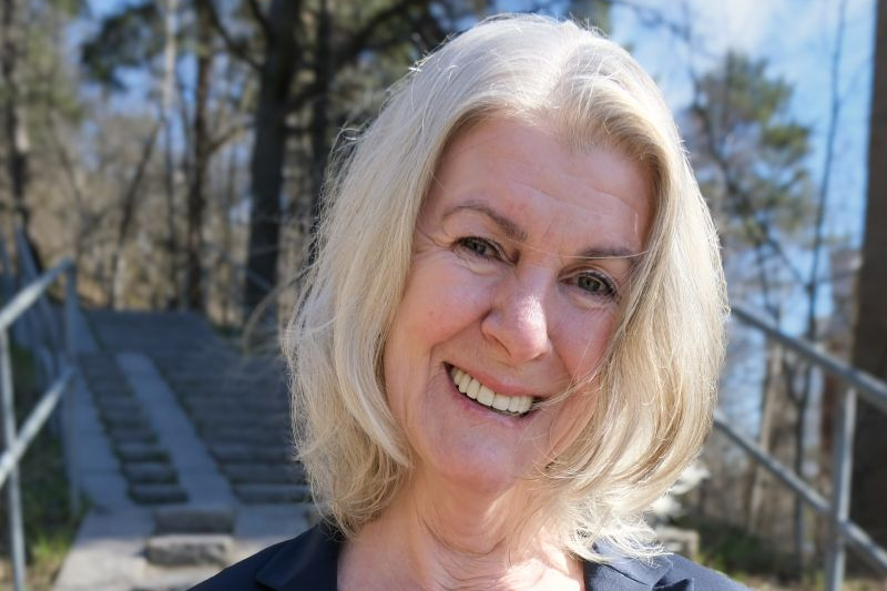 En kvinna i kavaj står i en trappa utomhus och ler.