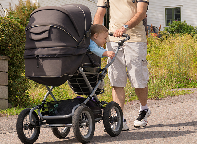 En pappa med barnvagn i sommarlandskap.