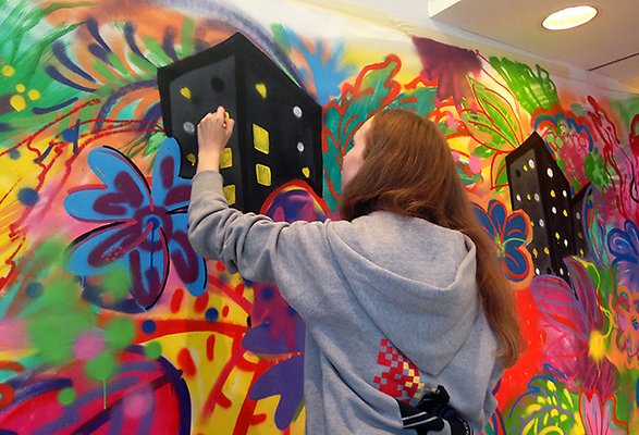 Ung kvinna målar med många färger på en vägg.