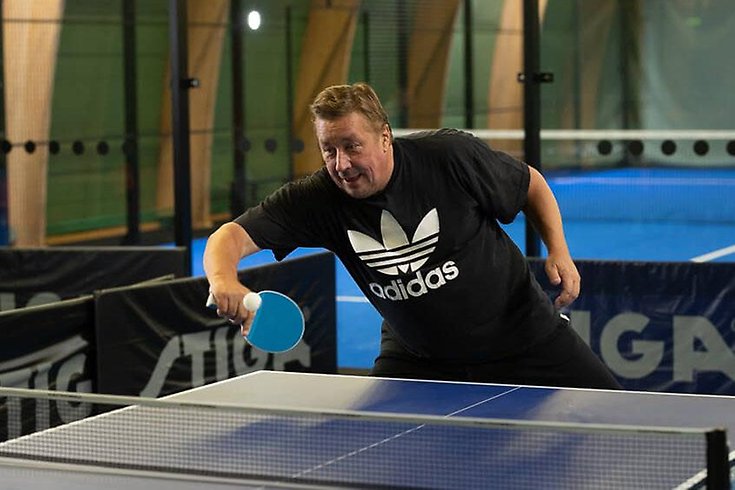 En man lutar över ett pingisbord med ett pingisracket i högsta hugg.