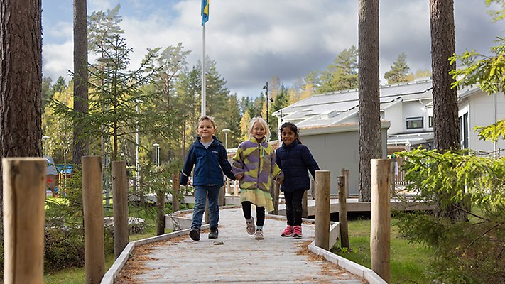 Tre barn springer på en träbro. 