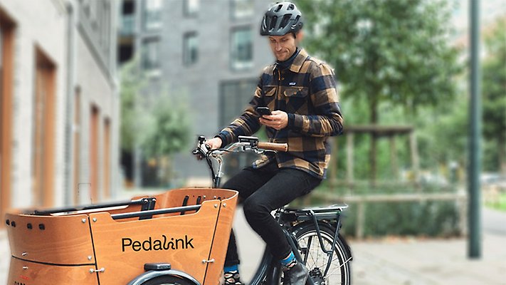 Bild på en man som sitter på en cykel med en lastlåda fram.